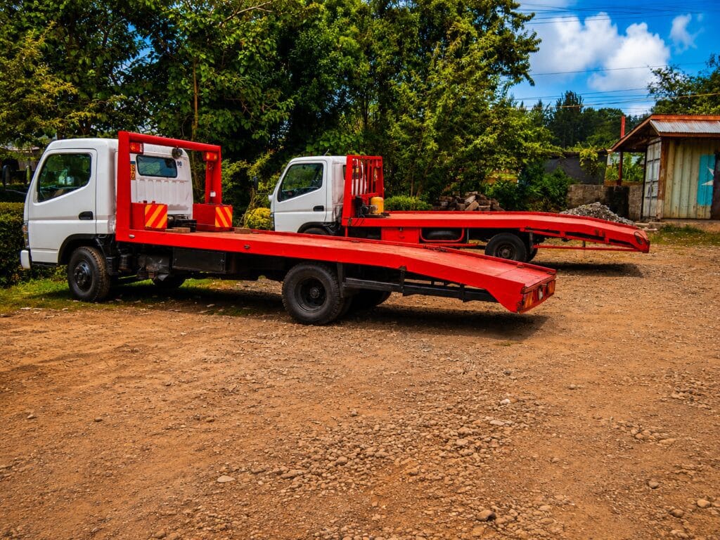 Two red flatbed tow trucks parked on a dirt lot