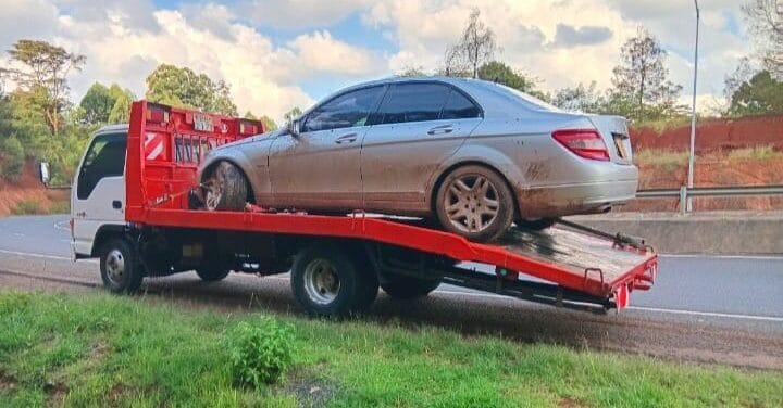Flatbed tow truck transporting a silver sedan securely on a highway